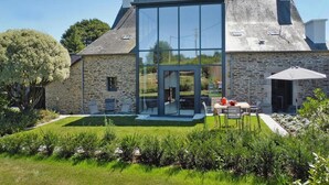 Une maison moderne dotée d’une véranda en verre, de murs en pierre et d’un jardin bien entretenu.