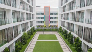 En moderne bygning med flere etager, store vinduer og en central gårdsplads med græs og beplantning.