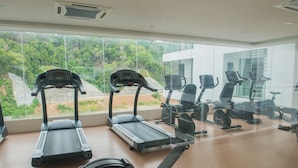 Et fitnesscenter med løbebånd og træningscykler, store vinduer med udsigt til grønne omgivelser.
