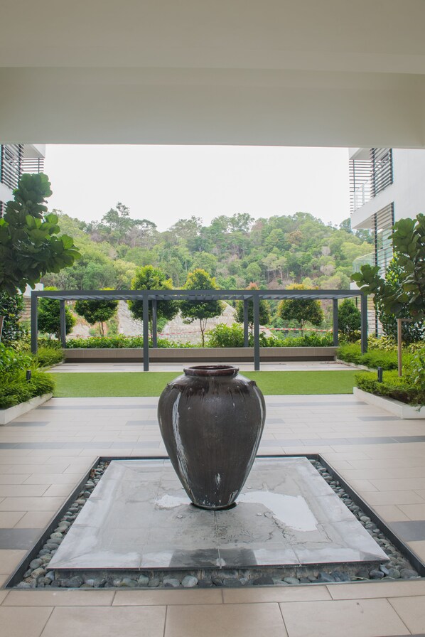 Surrounded by lush greenery, this tranquil outdoor space features a central urn on a tiled platform, set within a modern metal enclosure.