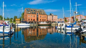 Un port de plaisance avec des bateaux amarrés, un grand bâtiment en briques et un ciel bleu dégagé.