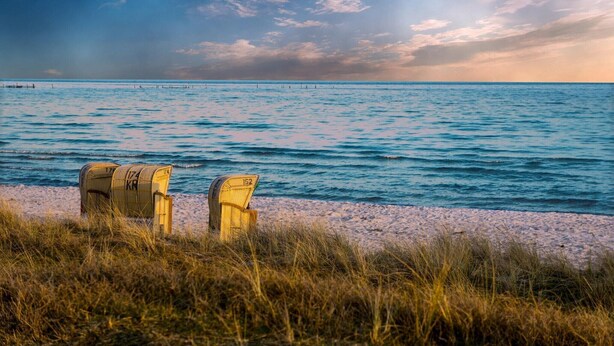 Une plage avec deux chaises en osier donnant sur la mer, un rivage sablonneux et une jetée au loin.