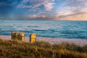 A beach with two wicker chairs facing the sea, a sandy shore, and a distant pier.