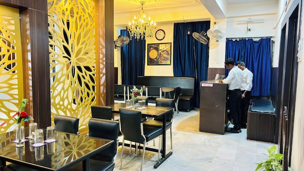 A restaurant with a modern interior, featuring a chandelier, a dining area with tables and chairs, and a kitchen area with staff. - Hotel Holidei Inn (Golmuri)