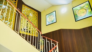 A staircase with a red handrail, decorative panels, and framed artwork on the walls. - Hotel Holidei Inn (Golmuri)