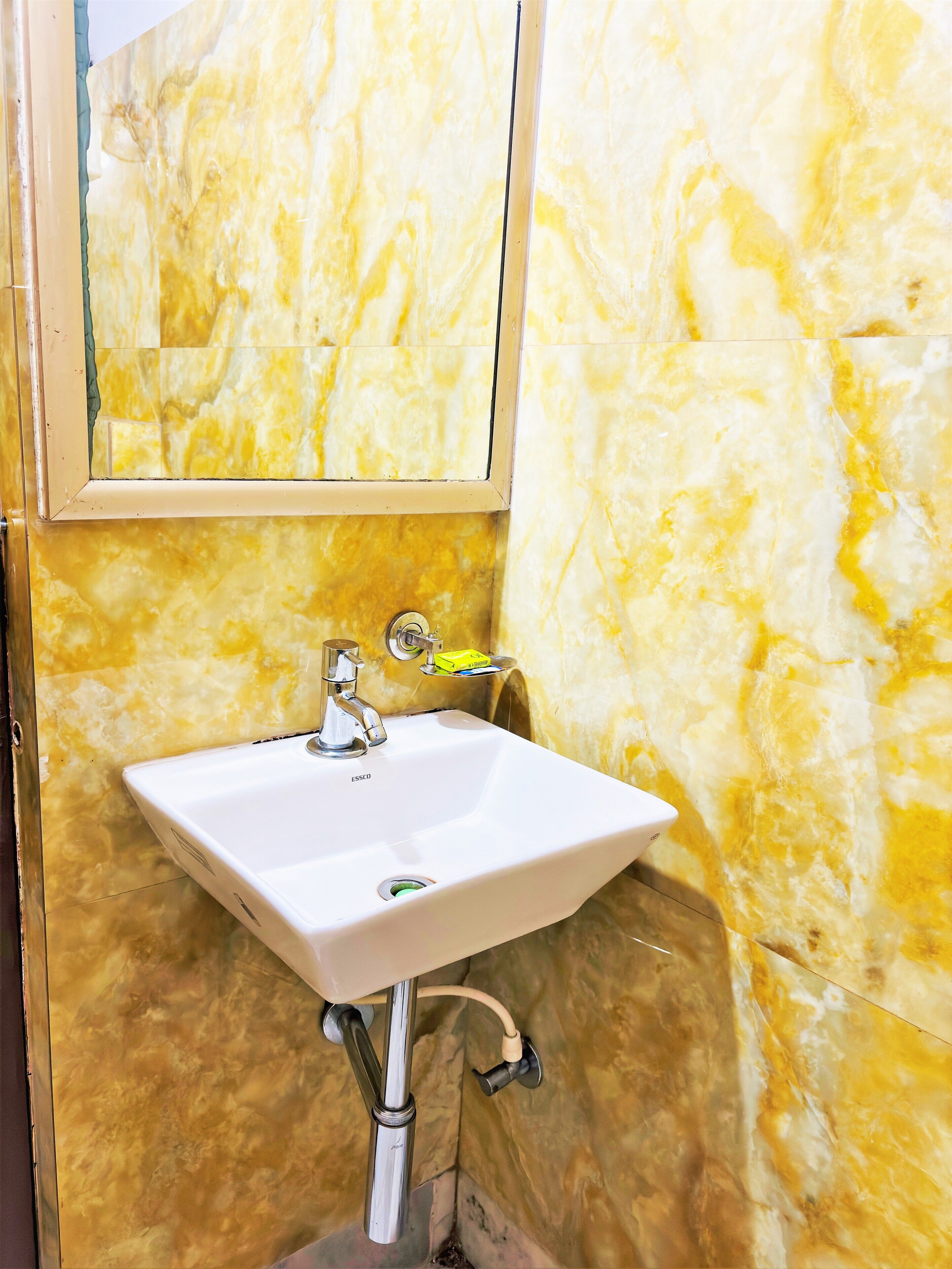 Un baño con lavamanos blanco, espejo y paredes de mármol amarillo.