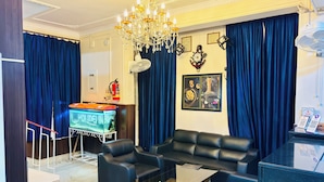 A modern living room with a chandelier, blue curtains, a fish tank, and a sofa. - Hotel Holidei Inn (Golmuri)
