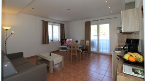 A compact living space with a sofa, dining table, chairs, a TV, and a kitchen area with a coffee maker and fruit. - Apartment in Zugspitz Arena near Highline 179 (Bichlbach)