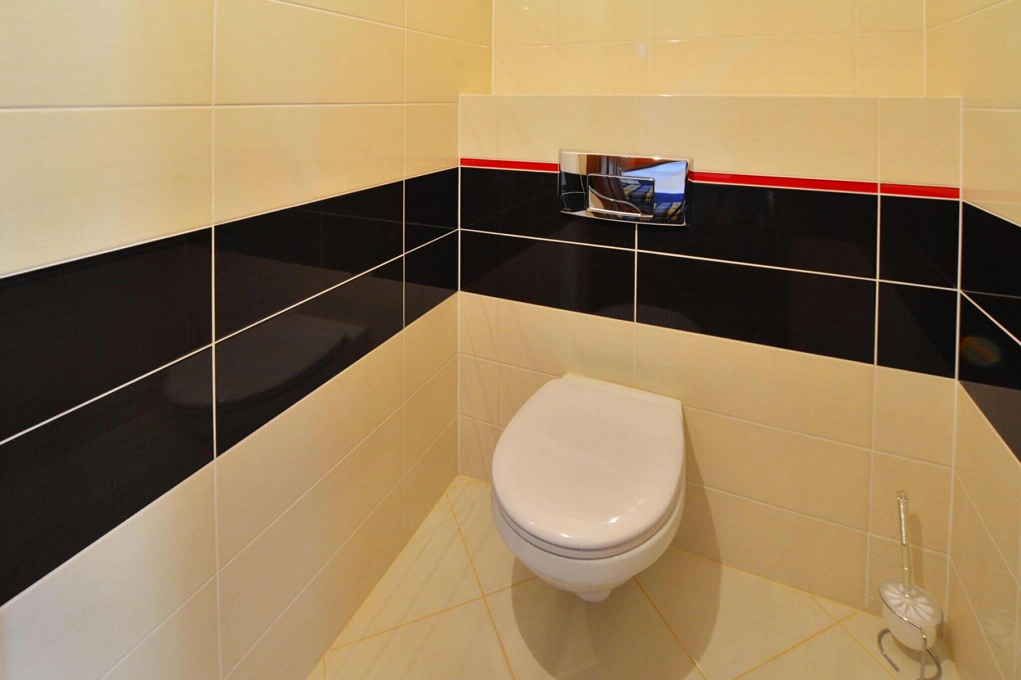 Et badeværelse med et hvidt toilet, vægge med sorte og hvide fliser og en rød stribe øverst.