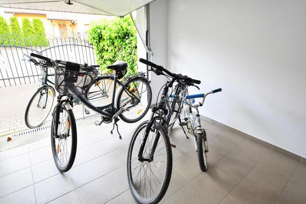 Two bicycles parked indoors with a tiled floor and a view of a garden outside.