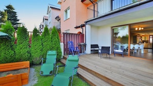 A wooden deck with outdoor seating, a barbecue grill, and a view of a modern building with large windows.