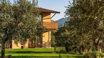 Una casa moderna con un balcone, immersa nel verde e con una montagna sullo sfondo.