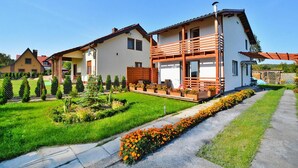 Una casa moderna de dos pisos con un balcón, un jardín cuidado y un cielo despejado.