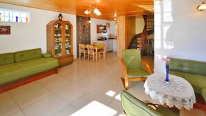 Una sala de estar acogedora con techo de madera, un sofá verde, una mesa de comedor con sillas y una cocina al fondo.