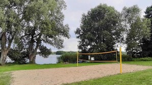 Una red de voleibol en un parque con una cancha de arena, rodeada de árboles y un lago.