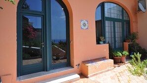 Un edificio con dos grandes ventanales arqueados, entrada con azulejos y plantas en macetas.