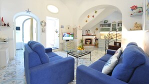 Una sala de estar con sofás azules, una mesa de centro y una chimenea. Hay un televisor y una escalera que lleva a otra habitación.