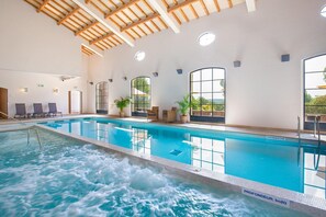 Una piscina interior con zona de jacuzzi, vigas de madera en el techo y amplias ventanas.