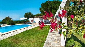 A swimming pool, a white building with arches, and red flowers.
