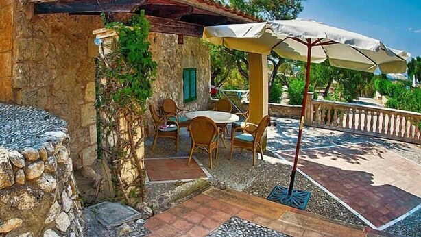 A stone building with a tiled patio, outdoor seating, and a pergola with an umbrella.