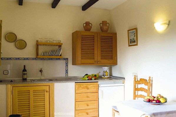 A kitchen with wooden cabinets, a sink, and a dining area with a table set for two. - Finca in Muro with Panoramic Views (Santa Margalida)