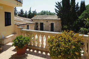 A building with a tiled roof, a balcony with a balustrade, and potted plants. - Finca in Muro with Panoramic Views (Santa Margalida)