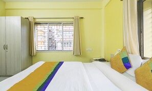 A hotel room with a bed, a wardrobe, a window with curtains, and a view of buildings outside. - Treebo Trip Flama House (Baruipur)