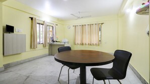 A conference room with a round table, four chairs, a ceiling fan, and a window with curtains. - Treebo Trip Flama House (Baruipur)