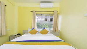 A hotel room with a bed, a nightstand, an air conditioner, and a window with curtains. - Treebo Trip Flama House (Baruipur)