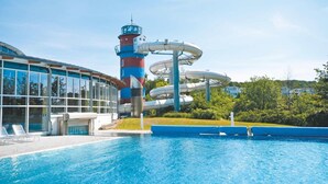 A swimming pool with a water slide and a building with large windows.