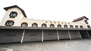Un bâtiment à la façade blanche et au toit brun, doté de nombreuses fenêtres et d’un espace d’entrée abrité.