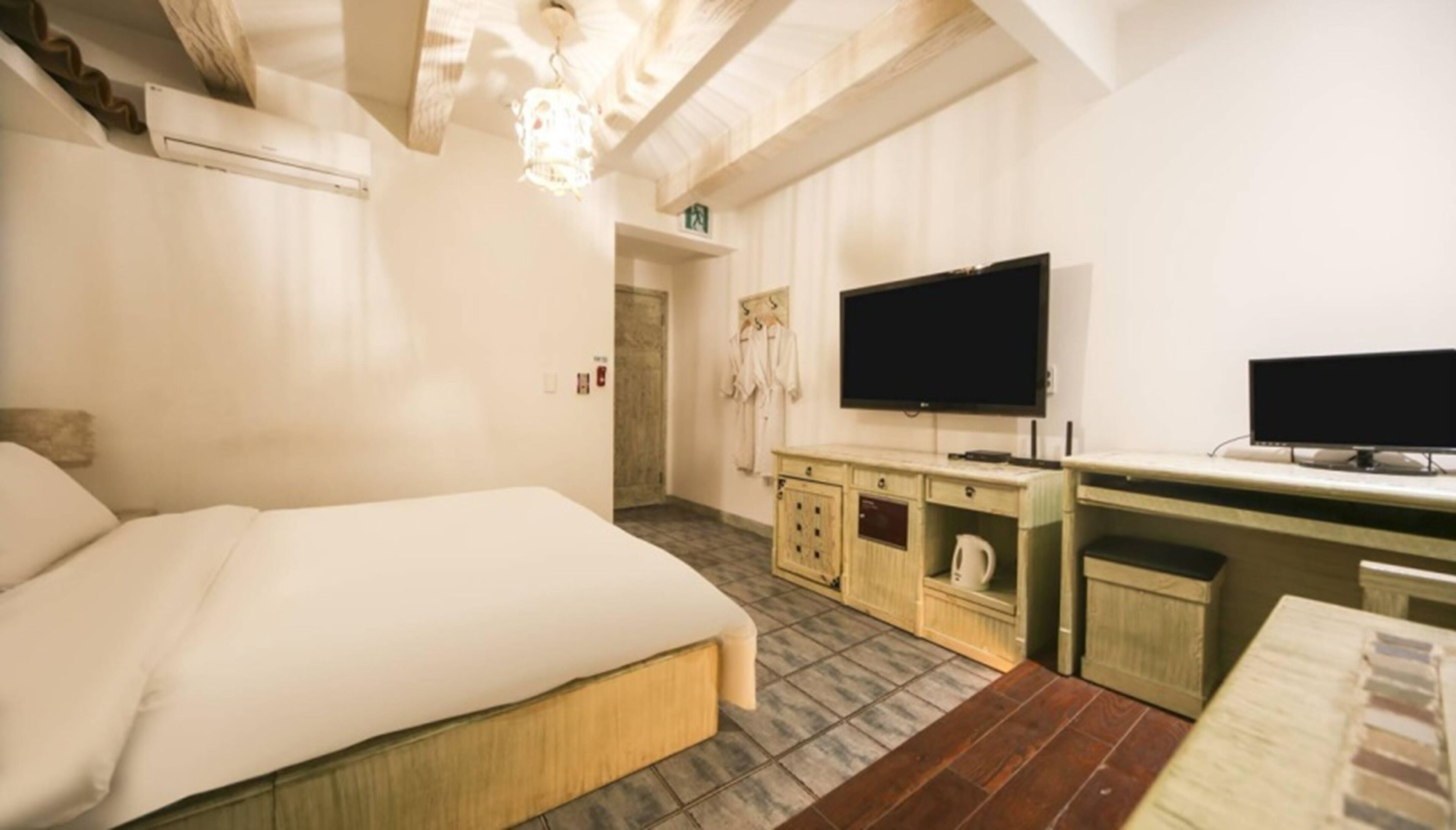 A hotel room with a bed, a television, a desk with a computer, and a kitchenette.