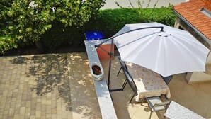 A patio area with a stone bench, a table, and a white umbrella. - Apartment in Starigrad Paklenica, National Park (Starigrad Paklenica)