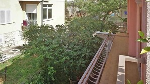 A balcony with a metal railing overlooking a garden with various plants and a building in the background. - Apartment in Starigrad Paklenica, National Park (Starigrad Paklenica)