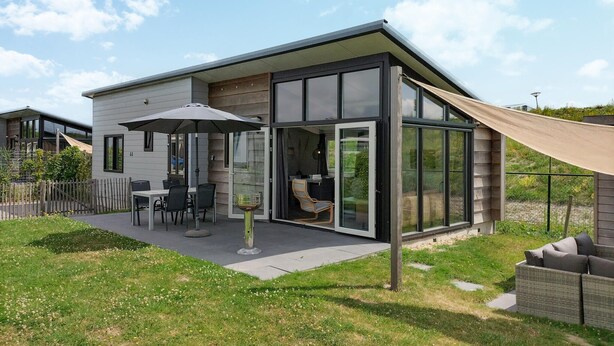 Een modern huis met een patio met een tafel en stoelen, een glazen deur die naar binnen leidt, en een groot raam.