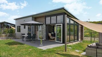 Una casa moderna con un patio attrezzato con tavolo e sedie, una porta in vetro che dà sull'interno e un'ampia finestra.