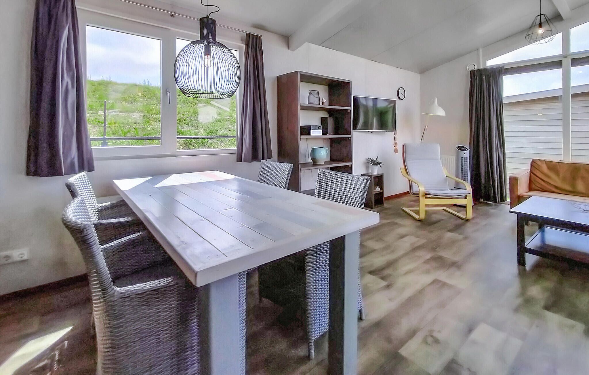 Zona pranzo moderna con tavolo in legno e sedie in vimini, una libreria, una TV e una poltrona dal design particolare.