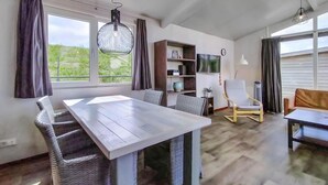 Een moderne eetruimte met een houten tafel en rieten stoelen, een boekenkast, een televisie en een stoel met een bijzonder design.