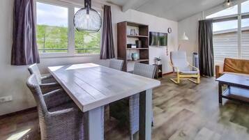 Zona pranzo moderna con tavolo in legno e sedie in vimini, una libreria, una TV e una poltrona dal design particolare.