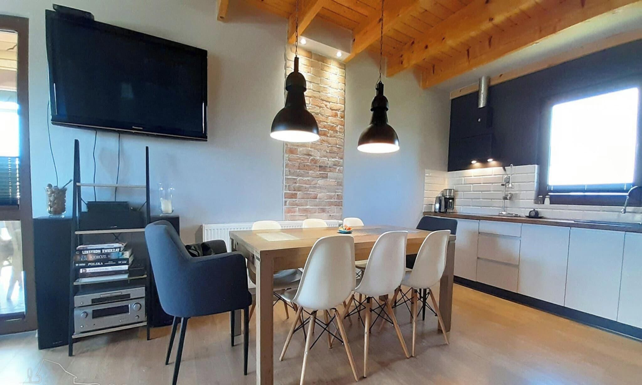 Une cuisine moderne avec un coin repas, des poutres apparentes en bois au plafond, un mur en briques et un téléviseur à écran plat.