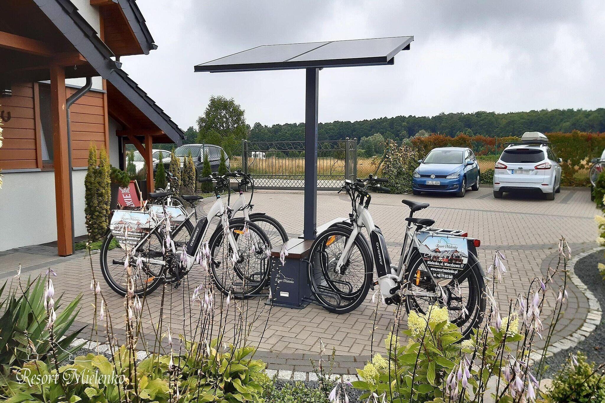 Un estacionamiento con bicicletas, automóviles, un panel solar y un edificio con fachada de madera.