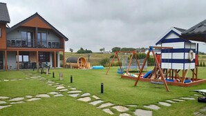 Uma casa moderna com varanda, um casebre de madeira e um trampolim no quintal.