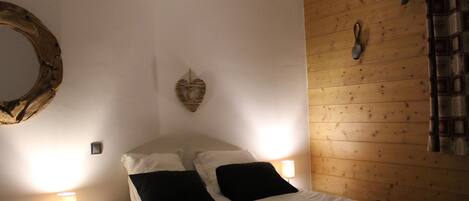 A bedroom with a wooden wall, a round mirror, a heart-shaped decoration, and two bedside lamps.