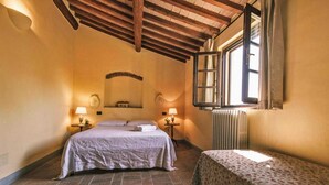 A bedroom with a bed, a small table, two lamps, a radiator, and a window with curtains. - Country House in Tuscany with Pool and Olive Grove (Santo Pietro Belvedere)