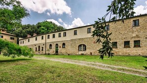 A courtyard with a stone building featuring arched windows and a central door. - Country House in Tuscany with Pool and Olive Grove (Santo Pietro Belvedere)