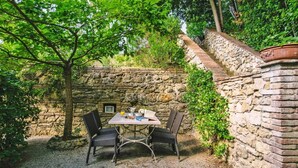 A stone wall with a table and chairs in a garden area. - Country House in Tuscany with Pool and Olive Grove (Santo Pietro Belvedere)