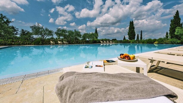 A poolside area with lounge chairs, a table with fruits and magazines, and a clear blue sky. - Country House in Tuscany with Pool and Olive Grove (Santo Pietro Belvedere)
