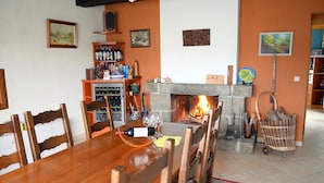 Un comedor con una mesa y sillas de madera, una chimenea encendida y una estantería para vinos con botellas.