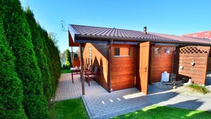 A wooden cabin with a tiled roof, a porch with seating, and a small shed. - Single-story, year-round holiday home (Ustronie Morskie)