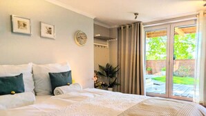 A bedroom with a large bed, a wall clock, framed pictures, a potted plant, and a sliding glass door leading to an outdoor area. - Spacious holiday apartment with sauna, Kolobrzeg (Kolobrzeg)